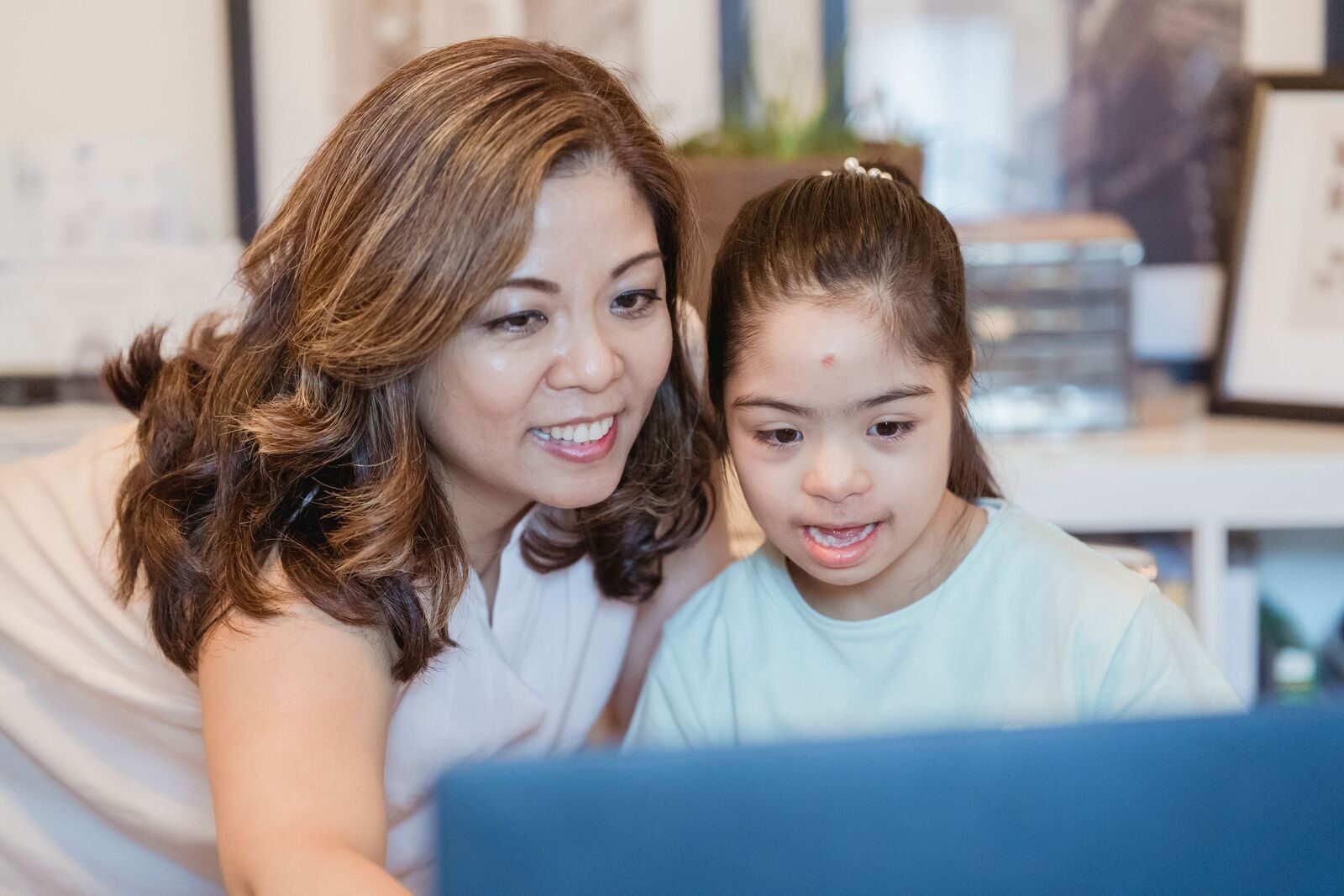 An educator and a young girl with Down syndrome smiling while learning together on a laptop