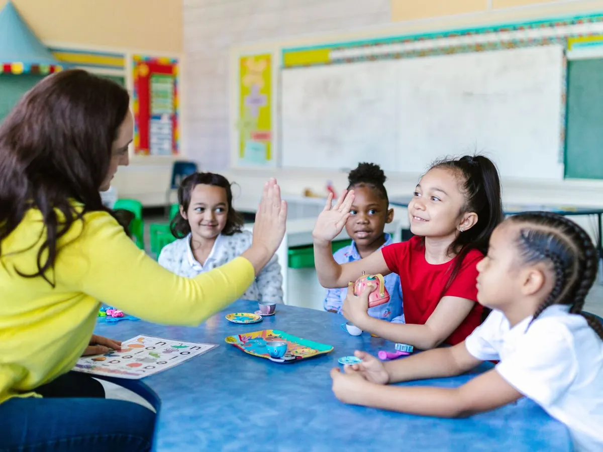 A teacher high-fives a student at a busy classroom table