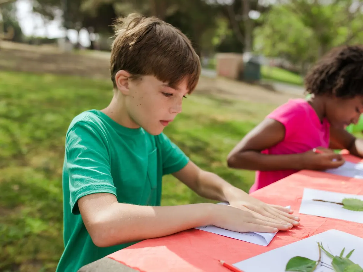 Children make leaf crafts at an outdoor table at summer camp