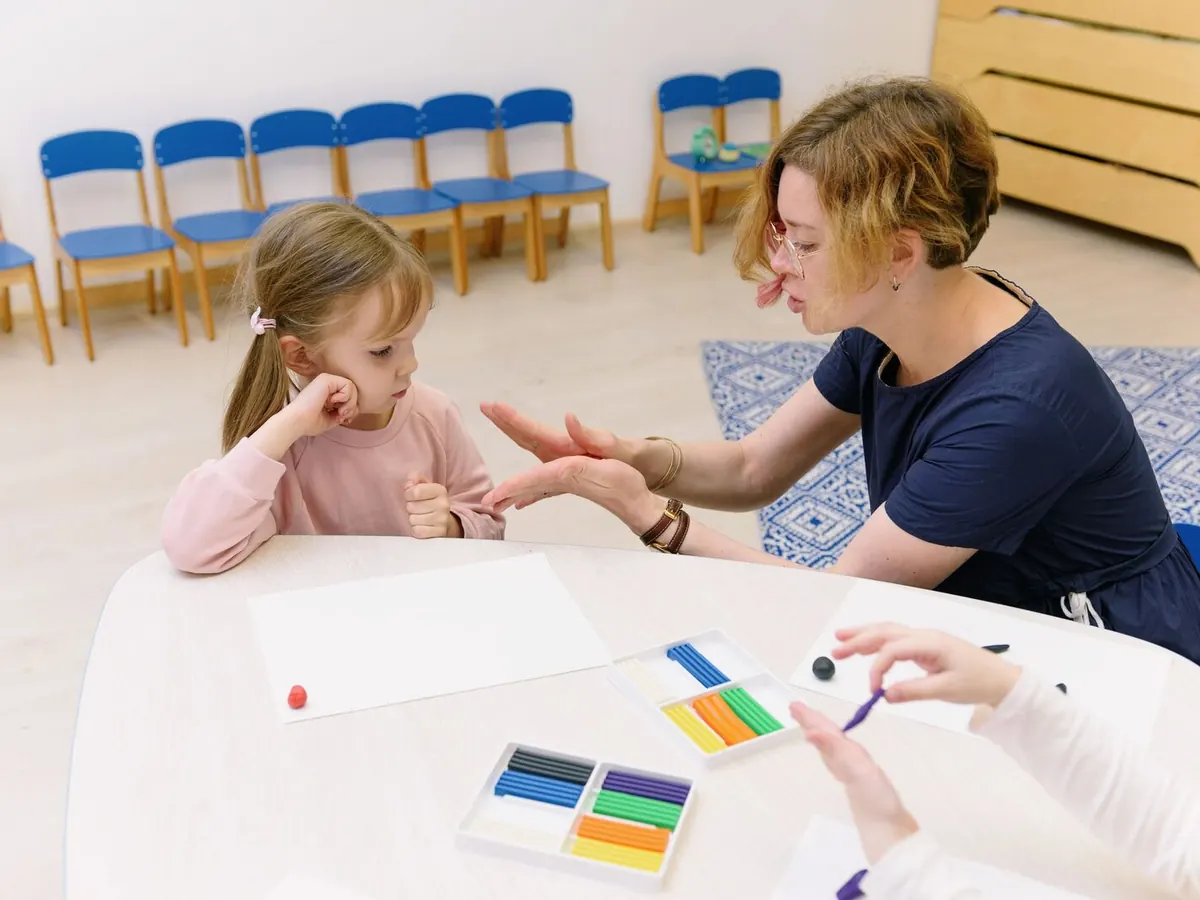 A specialist works with a young child at a table of colorful modeling clay